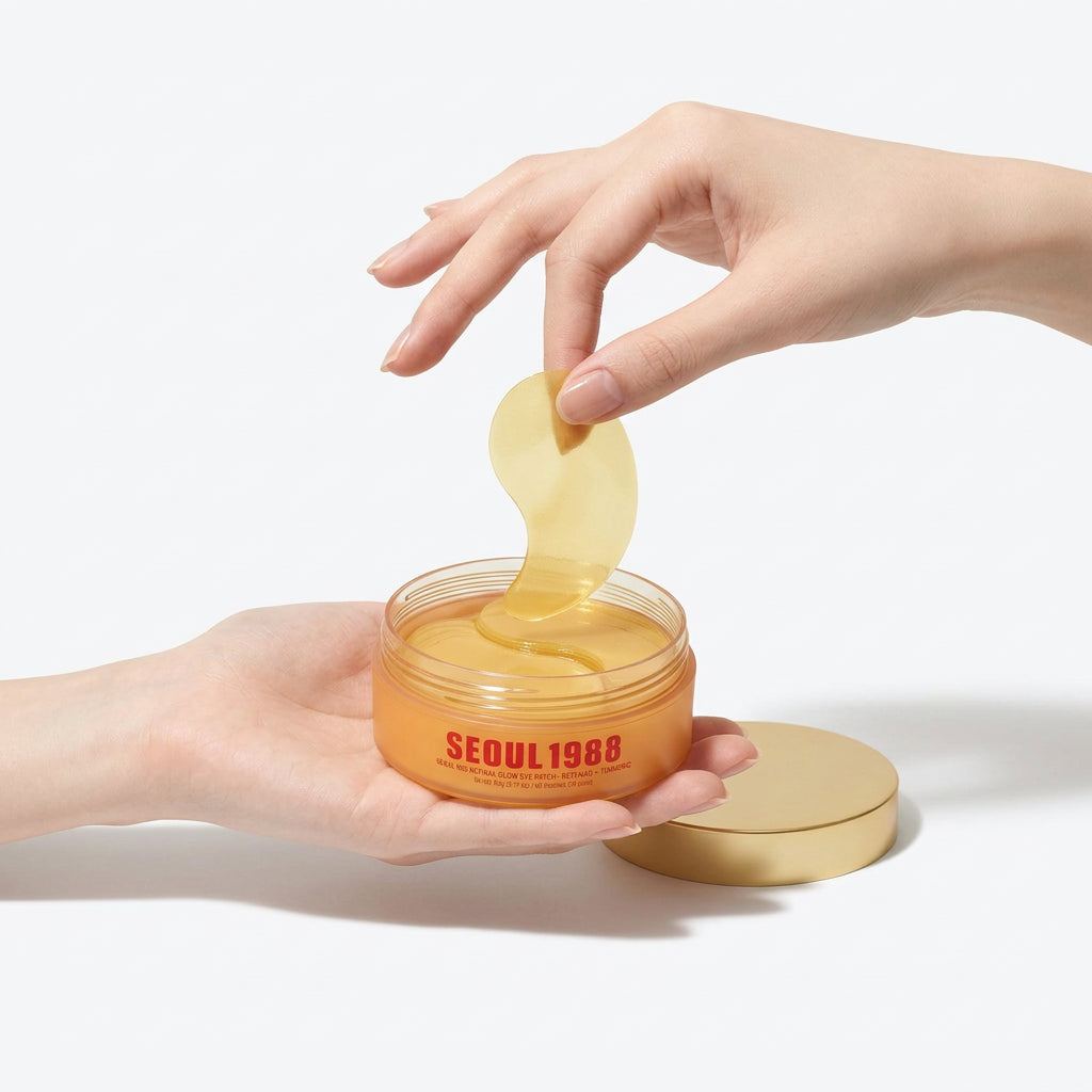 A hand holds an open jar of yellow skincare cream while another hand lifts a translucent yellow patch above it, against a clean light gray background. The jar is labeled SEOUL1988.